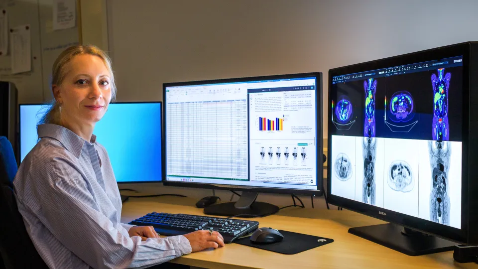 Kvinna i skjorta sittande vid två stora datorskärmar.